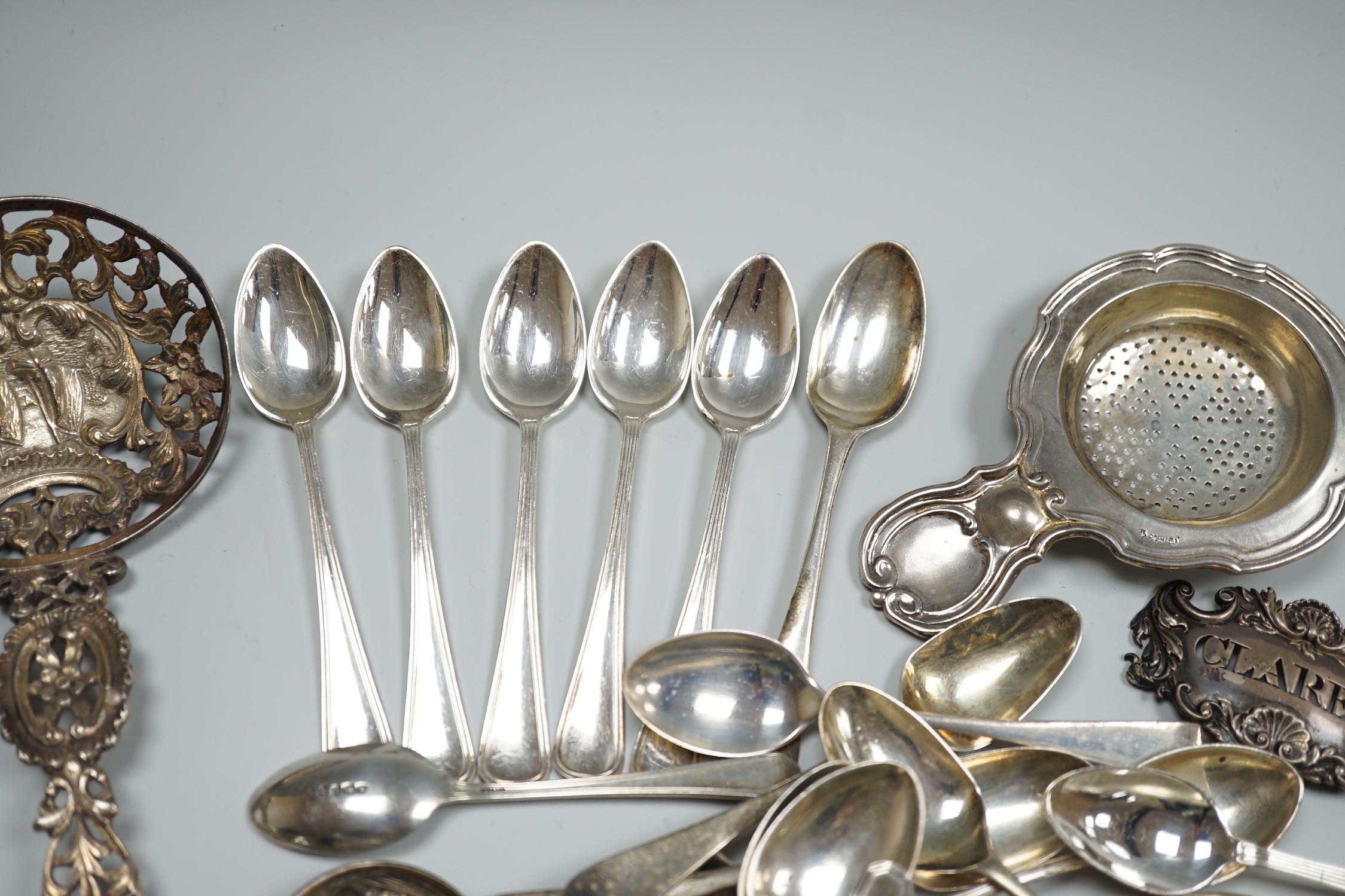 A group of mixed silver and white metal items including flatware, Dutch fish slice, German 800 tea strainer, George IV 'Claret' wine label, etc. and a plated spoon.